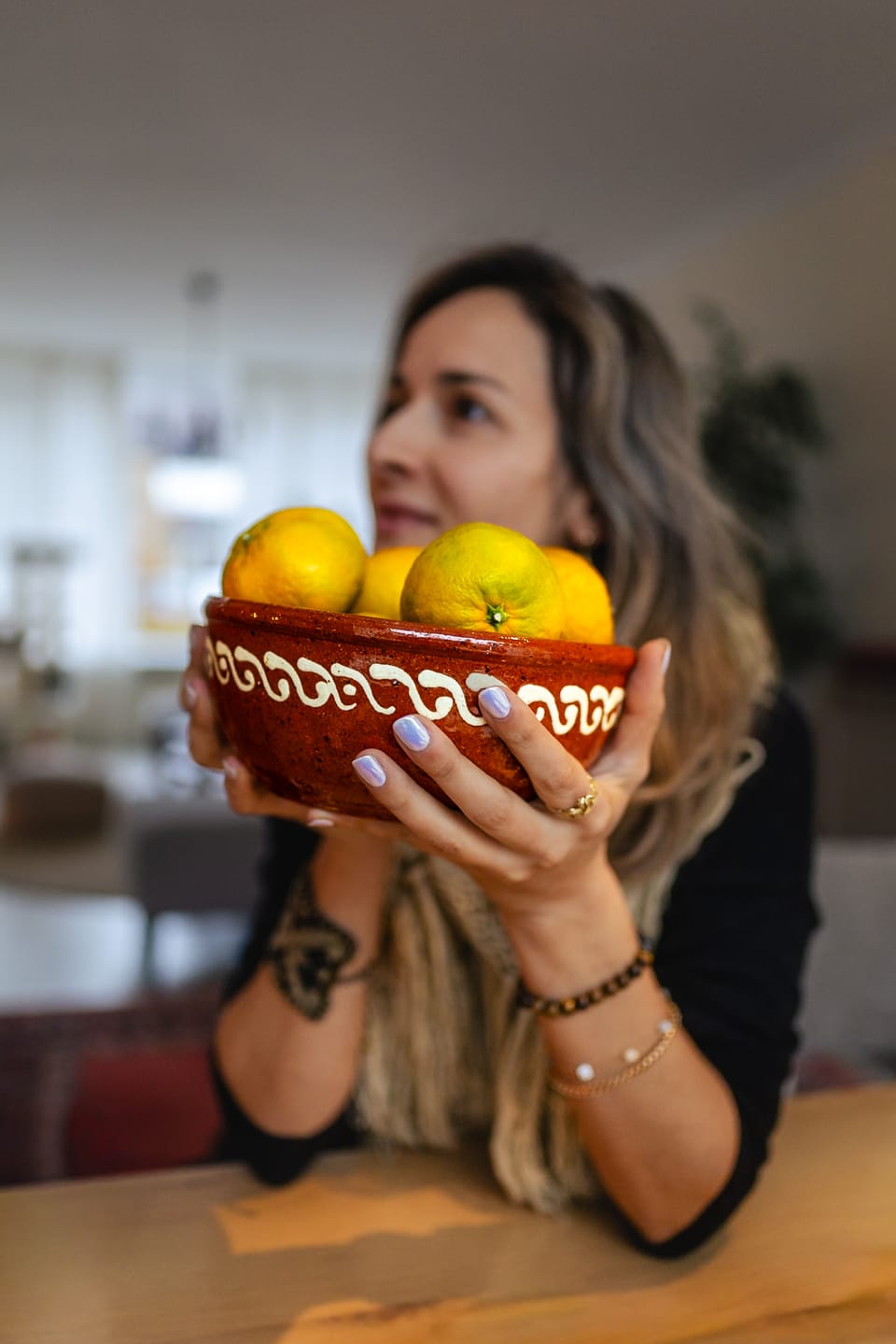 A woman holding a painted bowl of lemons in warm domestic light.