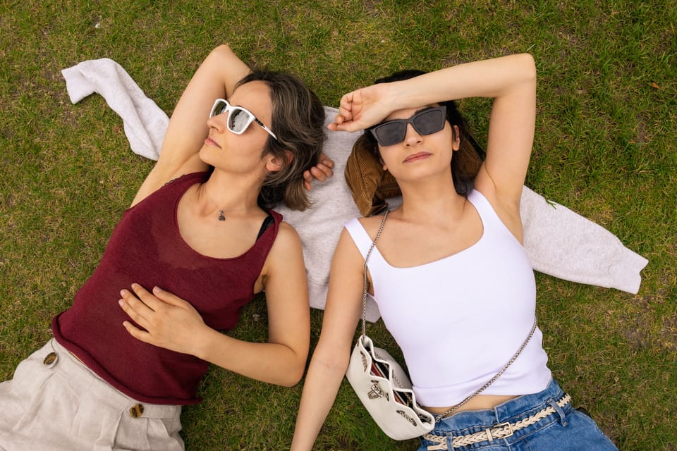 An overhead view of two women lying side by side on grass in summer.