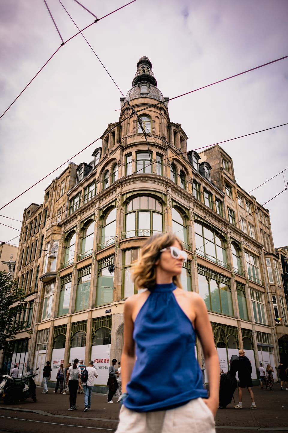 A woman in a blue halter top before an ornate corner building in Amsterdam.