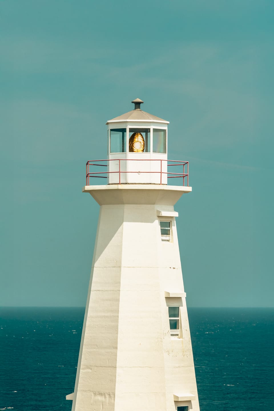 A white lighthouse standing against a deep teal sea at Cape Spear, Newfoundland.