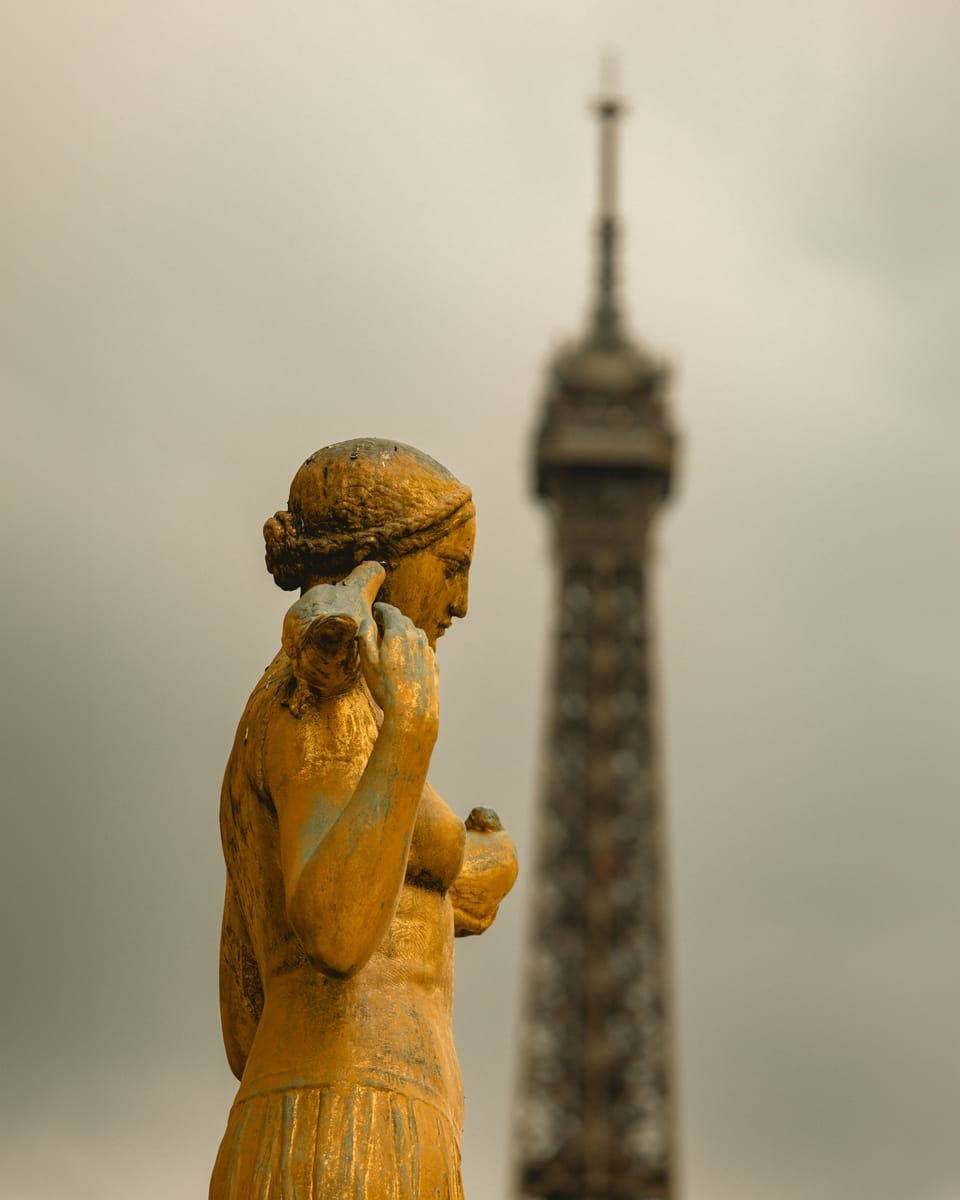 A golden statue in soft focus with the Eiffel Tower rising behind it.