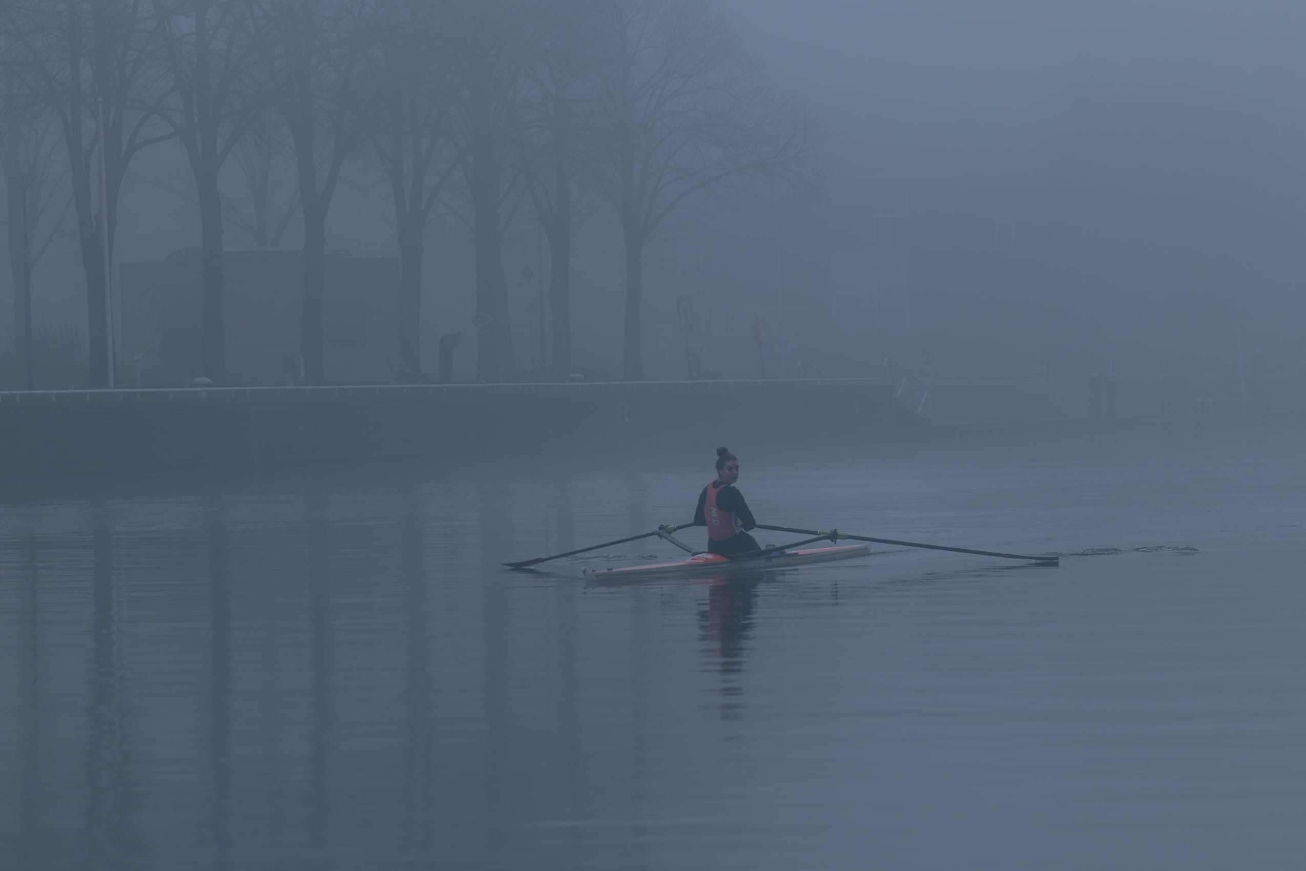 A lone rower gliding across still water through dense fog in Amsterdam.