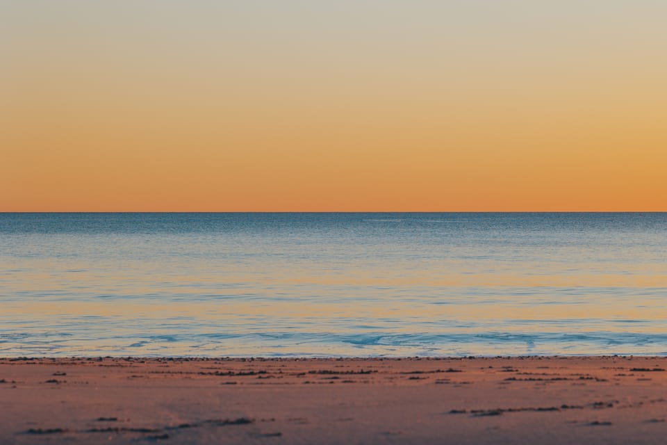 A minimal beach at dusk under a soft orange to blue gradient sky.