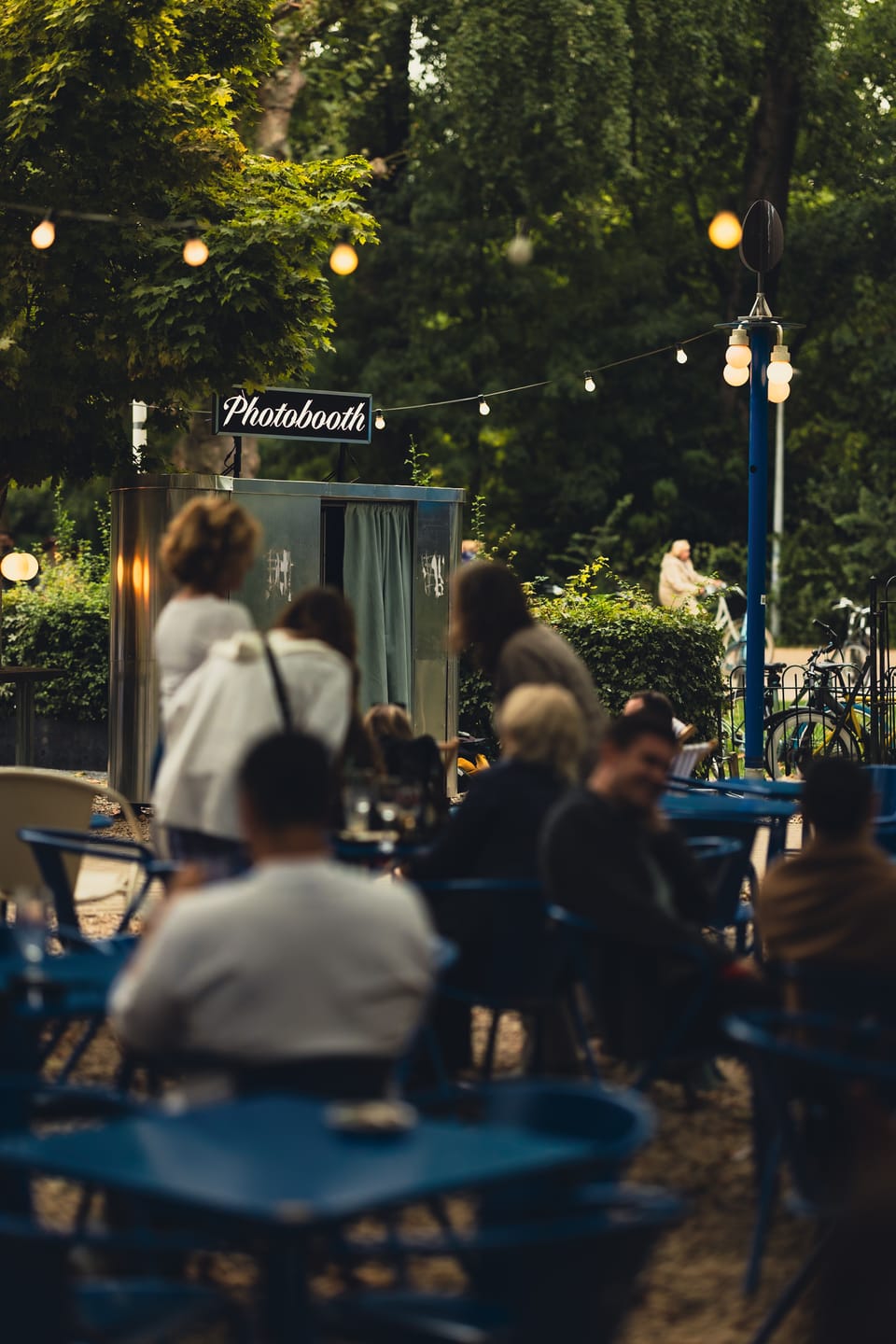An evening terrace crowd gathered around a photobooth beneath string lights.
