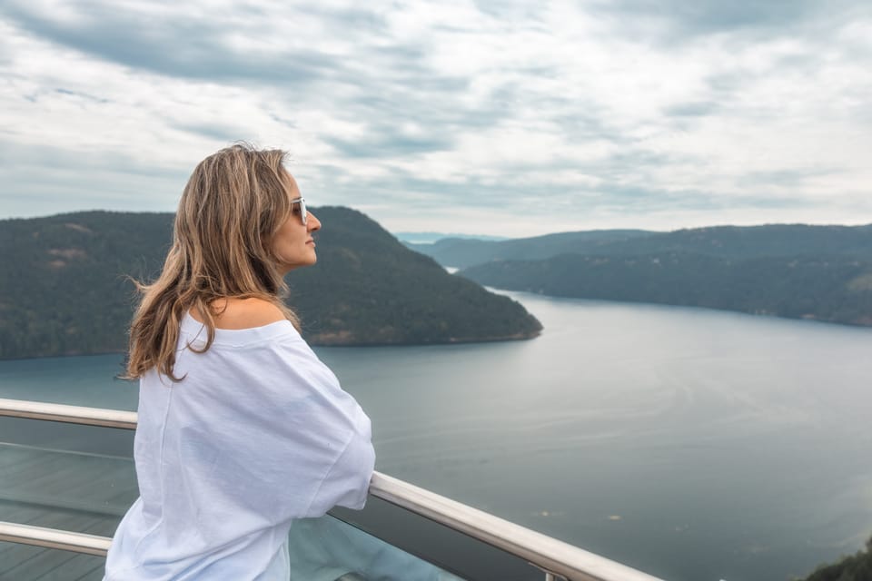 A woman in a white shirt looking out over a fjord from a boat deck.