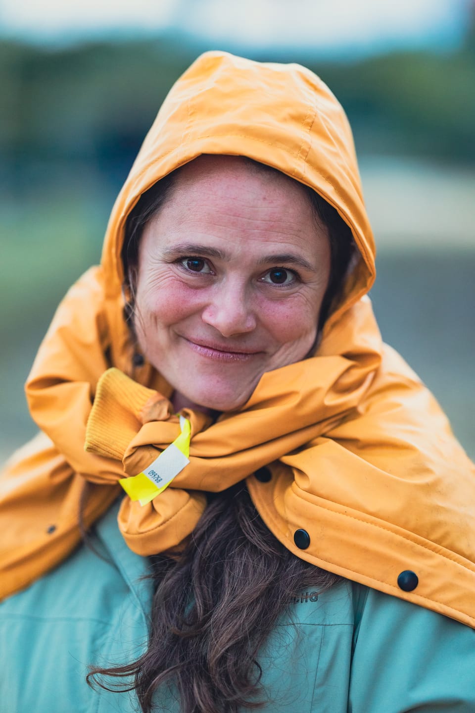 A close portrait of a woman smiling from inside a yellow rain hood.